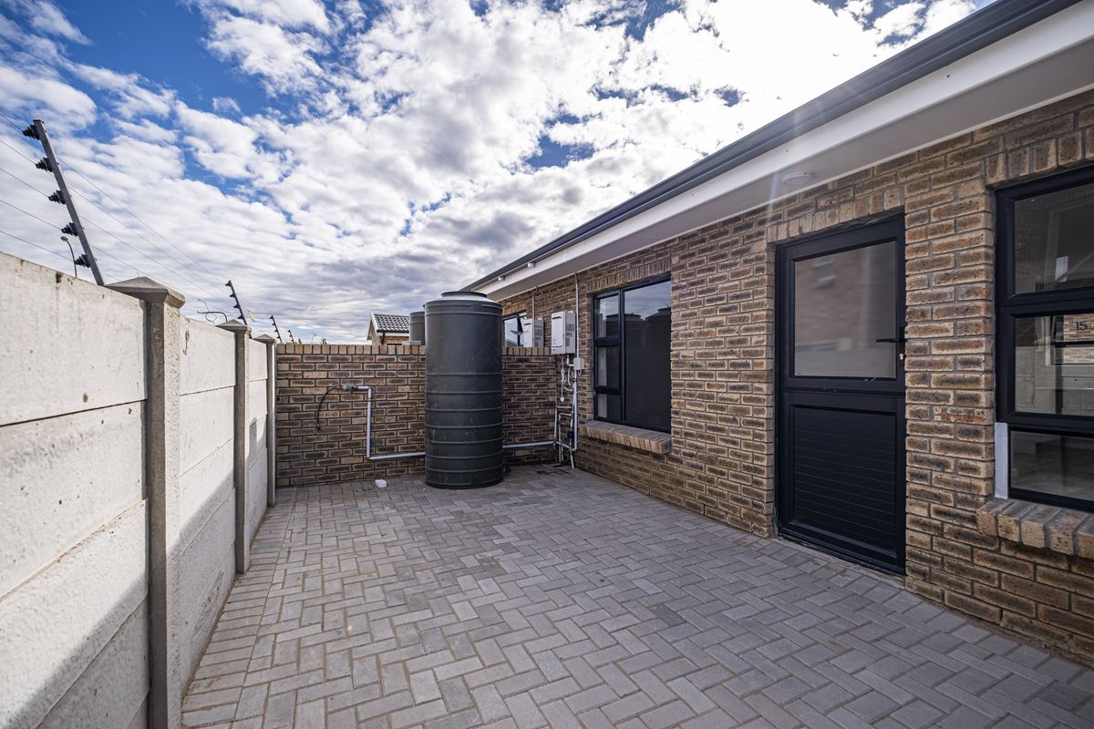 A paved rear courtyard featuring a brick exterior, a water storage tank, and an electric fence along the perimeter wall.