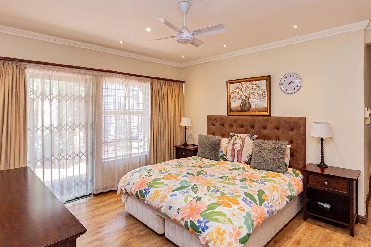 Spacious bedroom featuring laminate flooring, recessed ceiling lighting, a central ceiling fan, and sliding glass doors with security gates leading to the exterior.