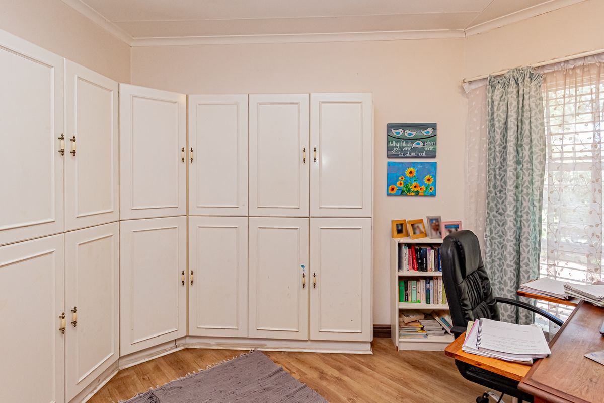 A functional bedroom featuring extensive built-in white cabinetry providing ample storage space, complemented by wood-look flooring and natural light.
