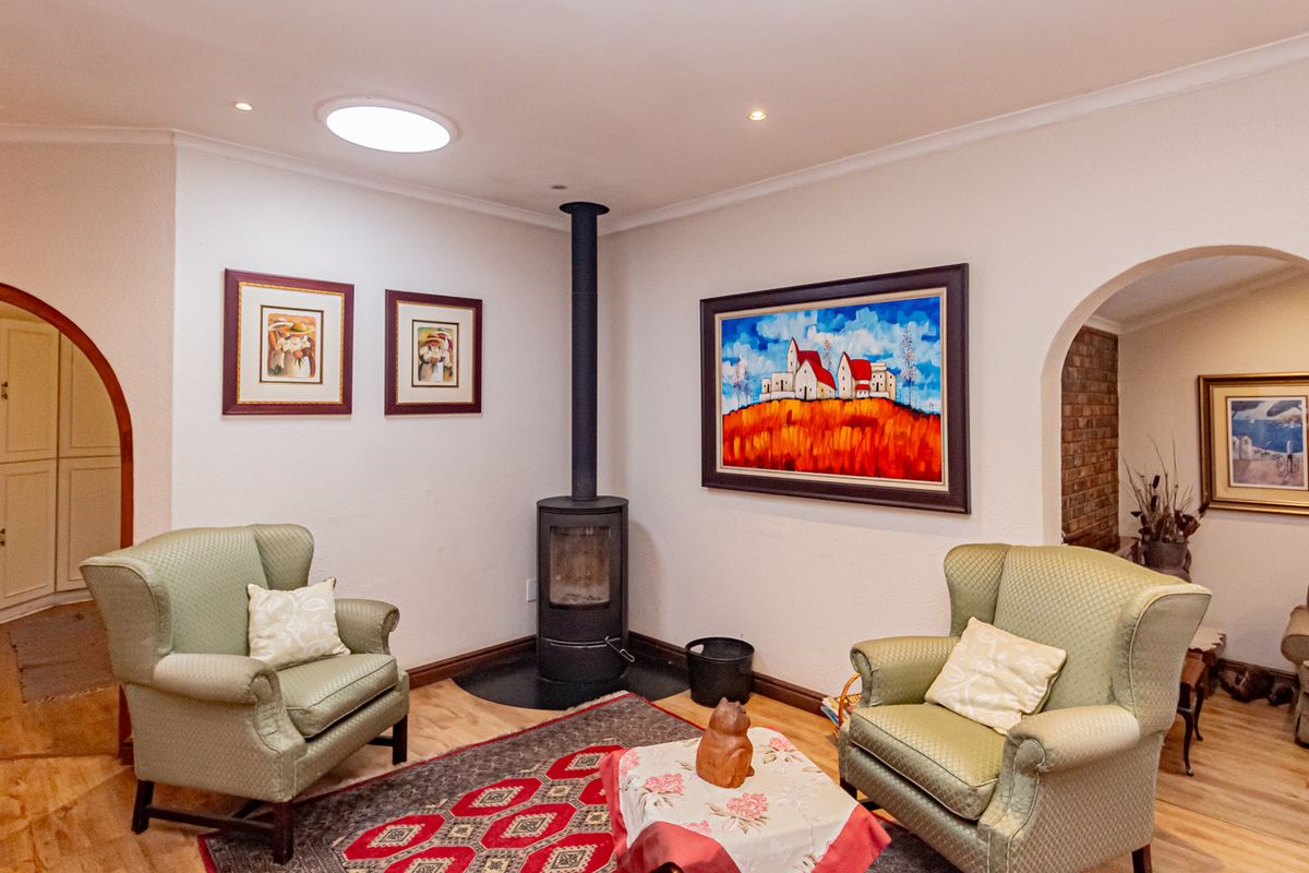 A cozy living room featuring a central freestanding wood-burning fireplace, recessed ceiling lighting, and a skylight, with arched doorways leading to adjacent spaces.
