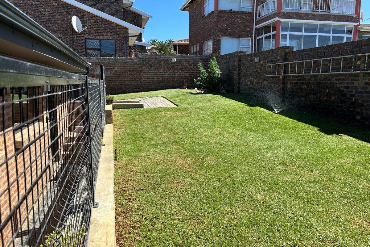 A private rear garden featuring a well-maintained lawn, paved section, and secure brick boundary walls.