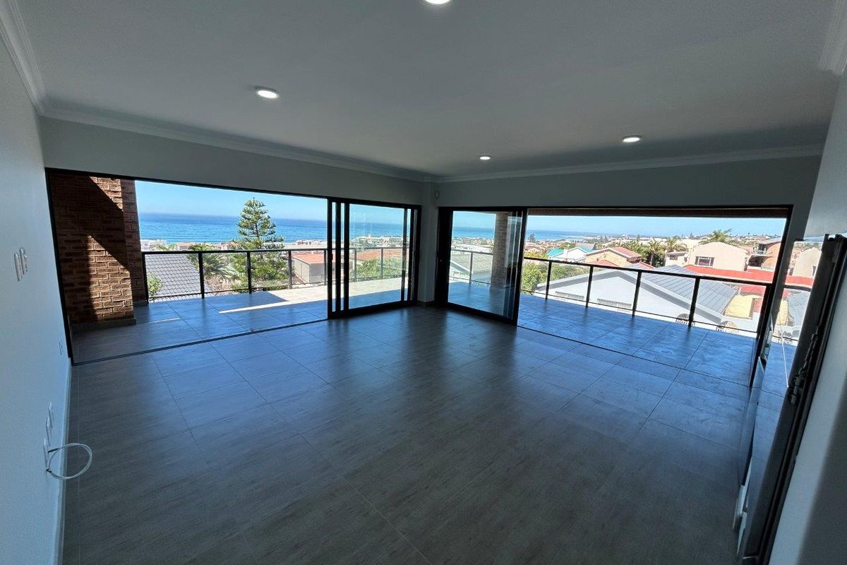 Spacious, modern open-plan living area featuring large sliding doors that open onto a balcony with expansive coastal and neighbourhood views.