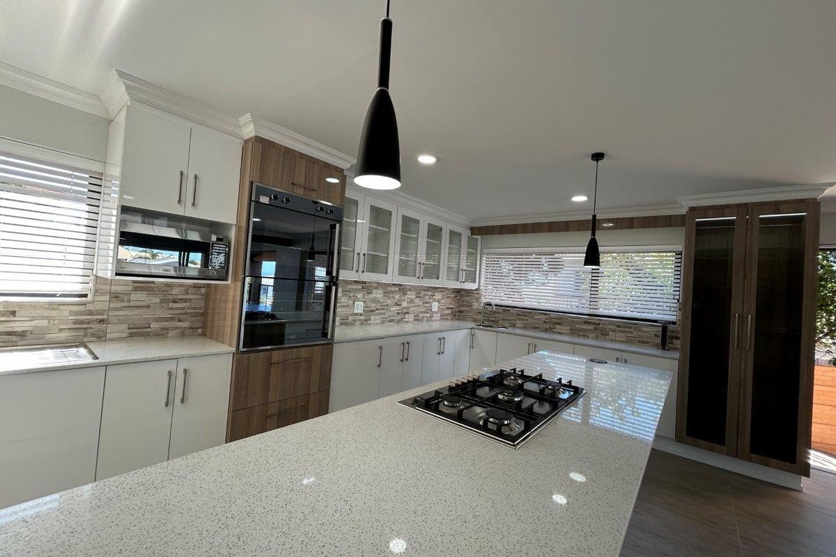 Modern kitchen featuring a large island with a gas cooktop, quartz countertops, built-in oven, microwave, and ample cabinetry with a stone tile backsplash.