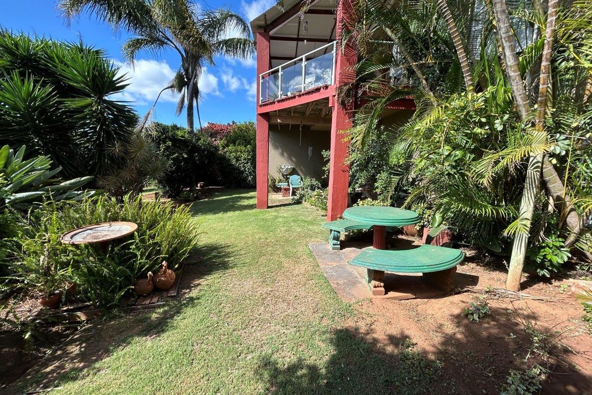A view of the rear garden featuring a lawn area, mature tropical landscaping, and a two-story structure with a covered patio and balcony.