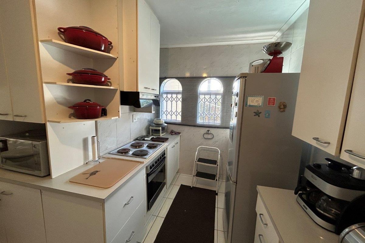Compact kitchen featuring white cabinetry, built-in oven and hob, extractor fan, and tiled flooring with arched windows.