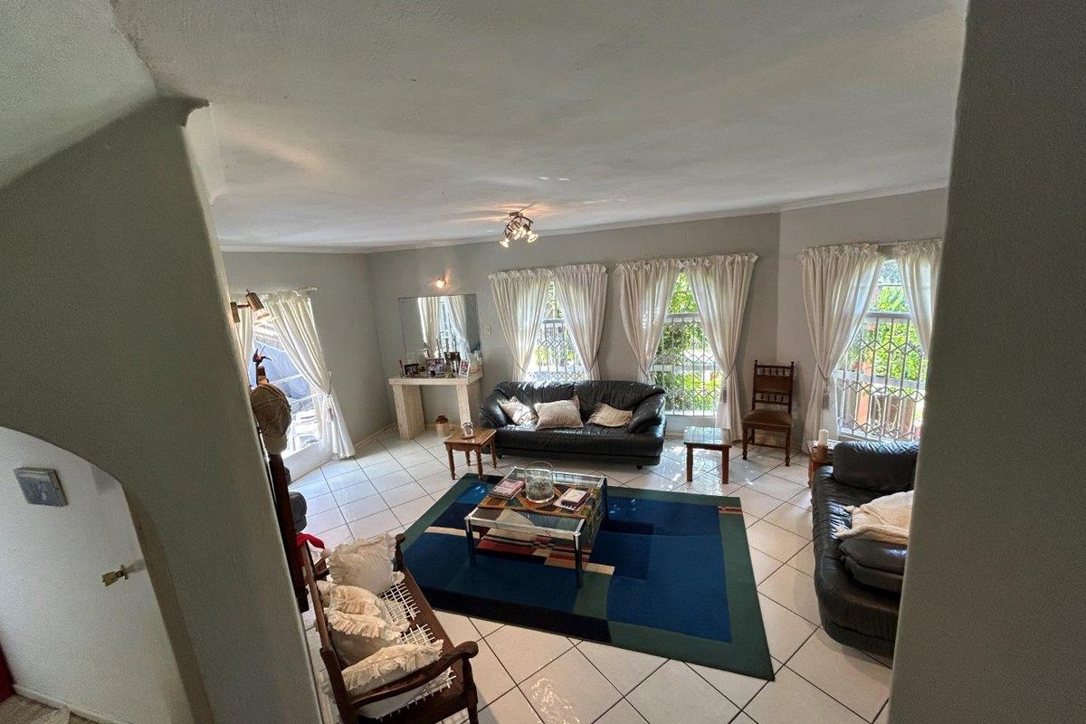 Spacious living room featuring large windows with security bars, tiled flooring, and a built-in console table.