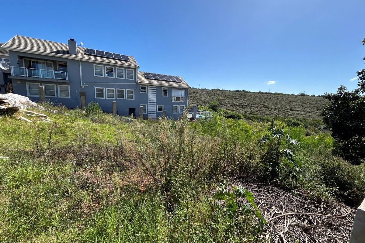 A view of the rear elevation of a residential property featuring solar panels, set against a backdrop of natural hillside terrain.
