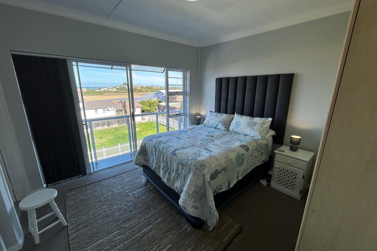 A bedroom featuring a large sliding glass door that opens onto a balcony with scenic coastal views.