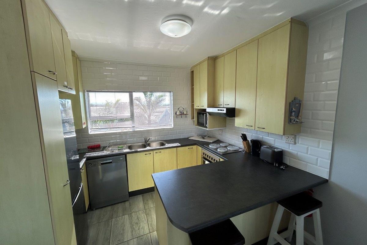 A functional kitchen featuring light-toned cabinetry, dark countertops, a double sink, subway tile backsplash, and a built-in hob with an extractor fan.