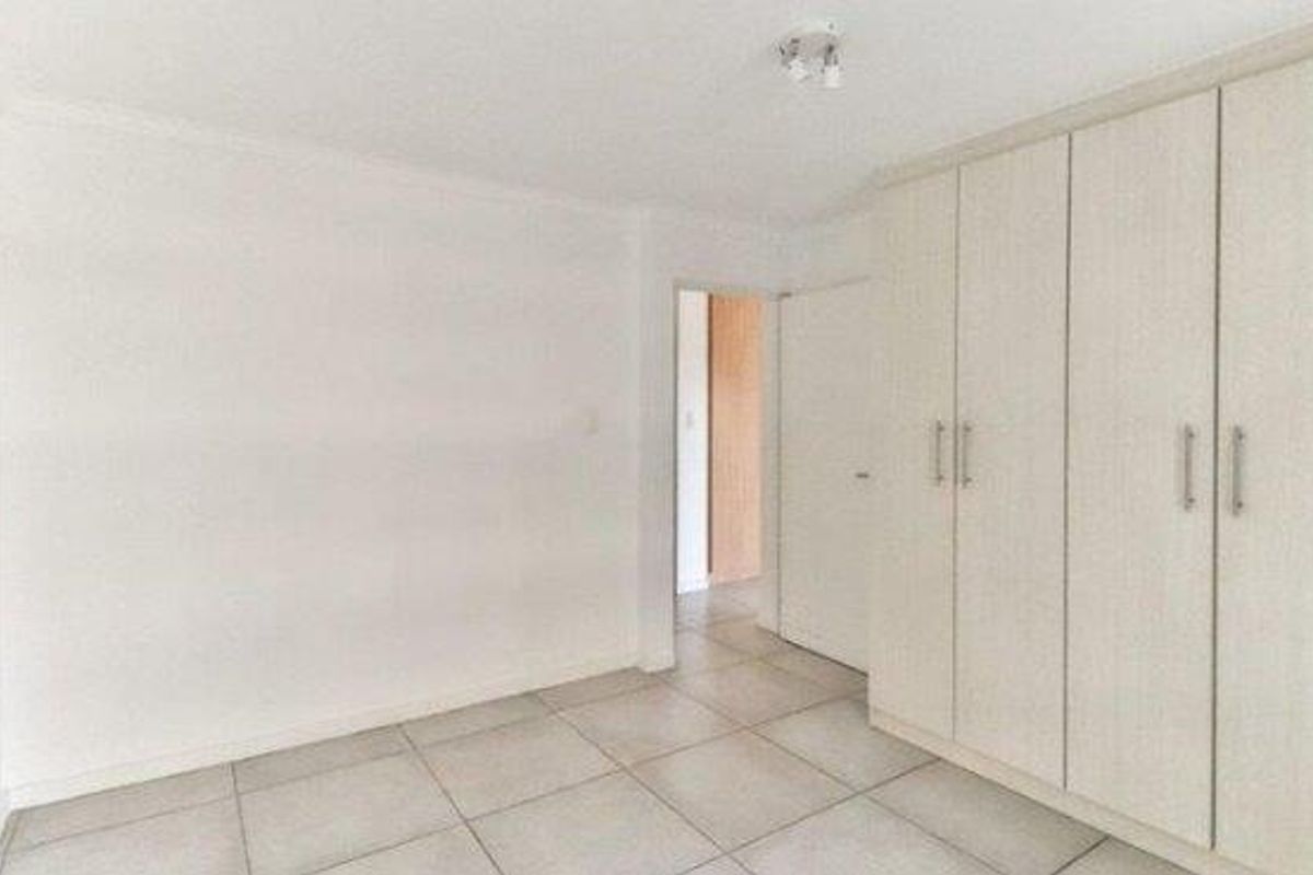A bright bedroom featuring neutral floor tiles and built-in cabinetry with light wood-grain finish.