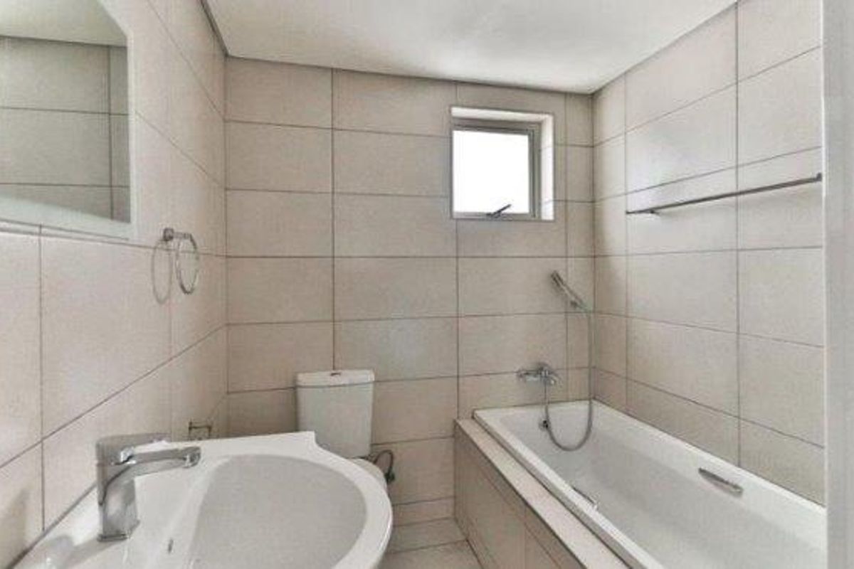 A functional bathroom featuring full-height wall tiling, a built-in bathtub with shower mixer, a pedestal basin, and a toilet.