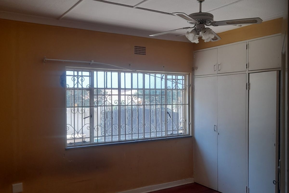 A bedroom featuring built-in cupboards, a ceiling fan, and security bars on the window, with wooden flooring throughout.