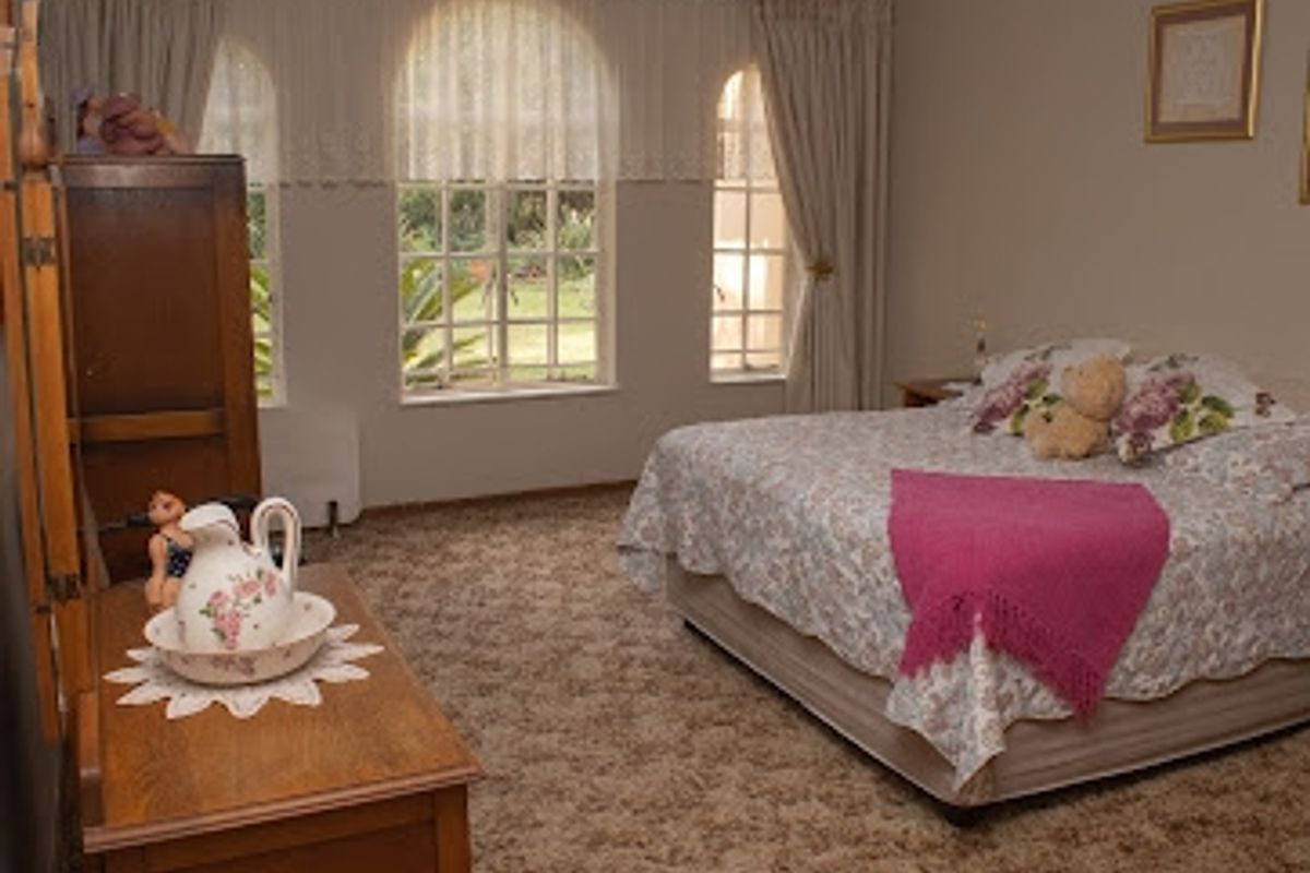 A spacious bedroom featuring large arched windows that provide natural light and views of the garden, finished with fitted carpeting.