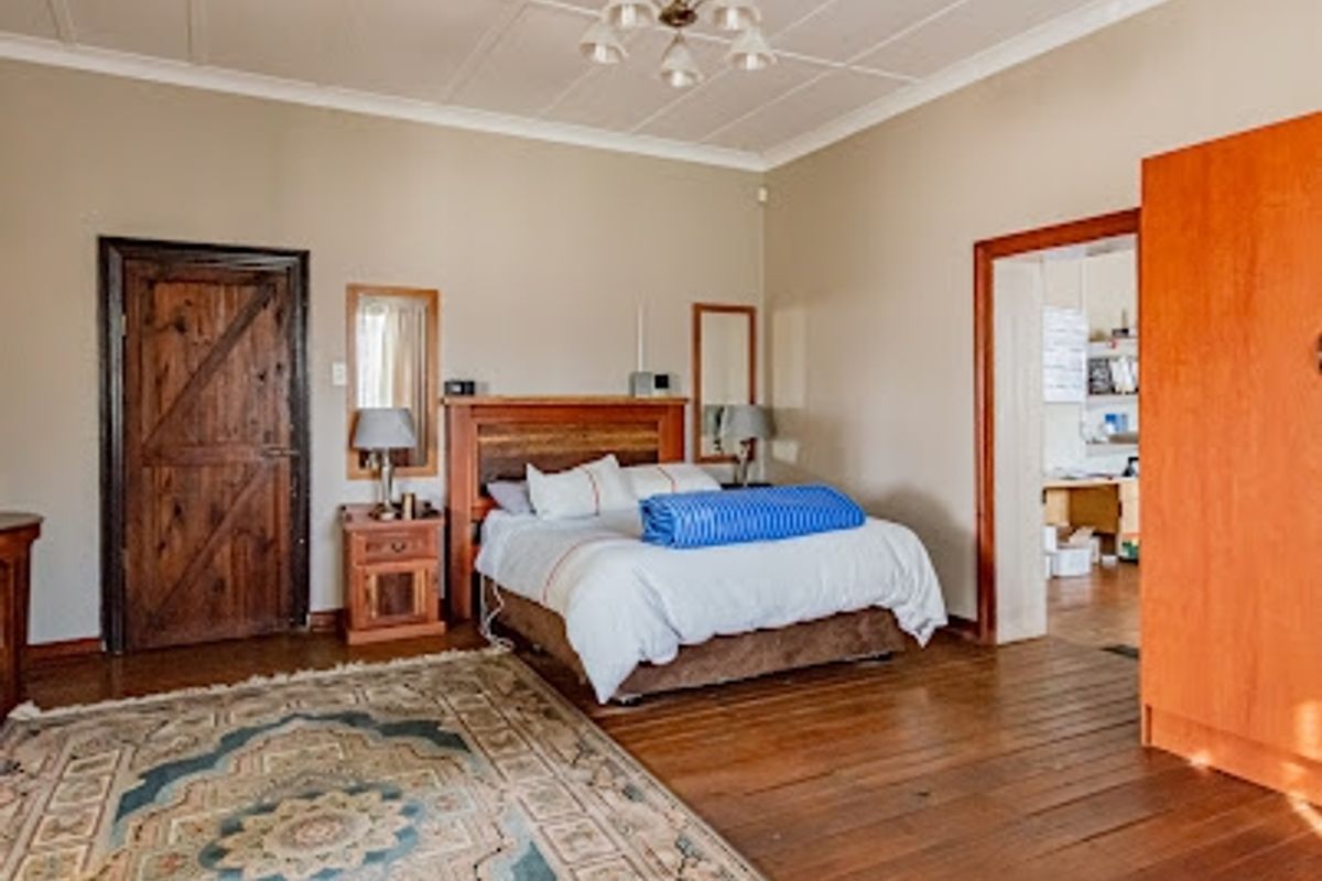 Spacious bedroom featuring original wooden flooring, a panelled ceiling, and a solid wood door, offering a rustic and character-filled living space.