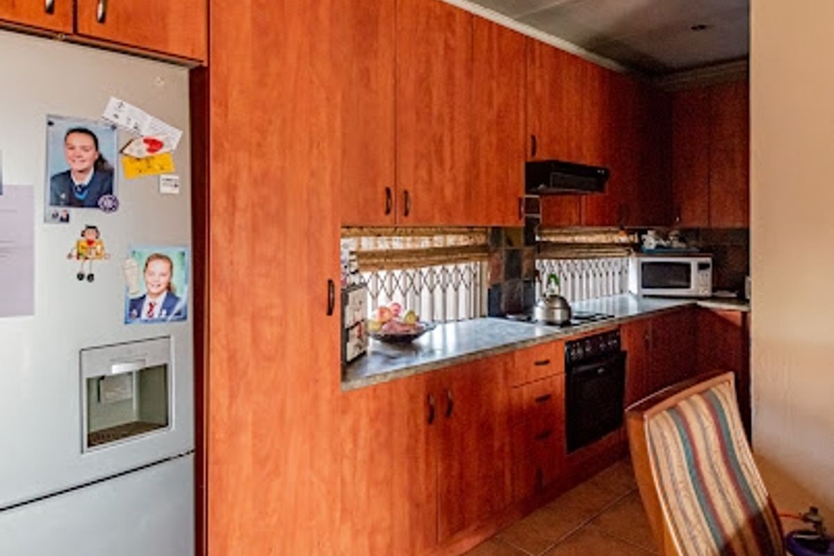 A functional kitchen featuring extensive wood-finish cabinetry, built-in oven and hob, tiled flooring, and a security gate over the window.