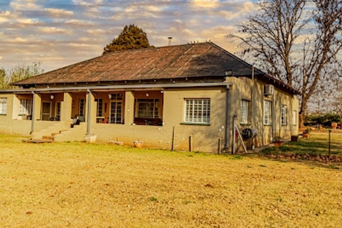 Rear view of a traditional small holding farmhouse featuring a covered patio, brick exterior, and a large corrugated metal roof.
