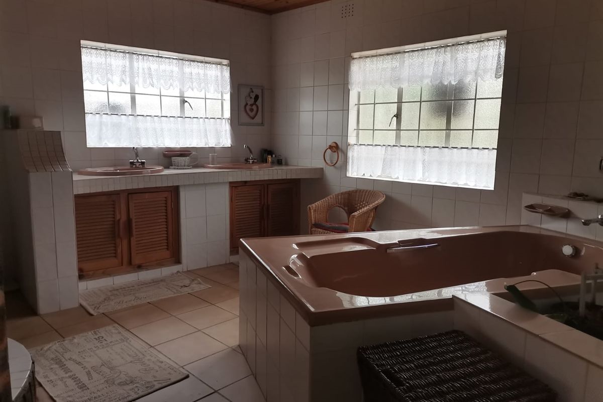 A spacious bathroom featuring a built-in tiled vanity with dual basins, a large sunken bathtub, and timber ceiling finishes.