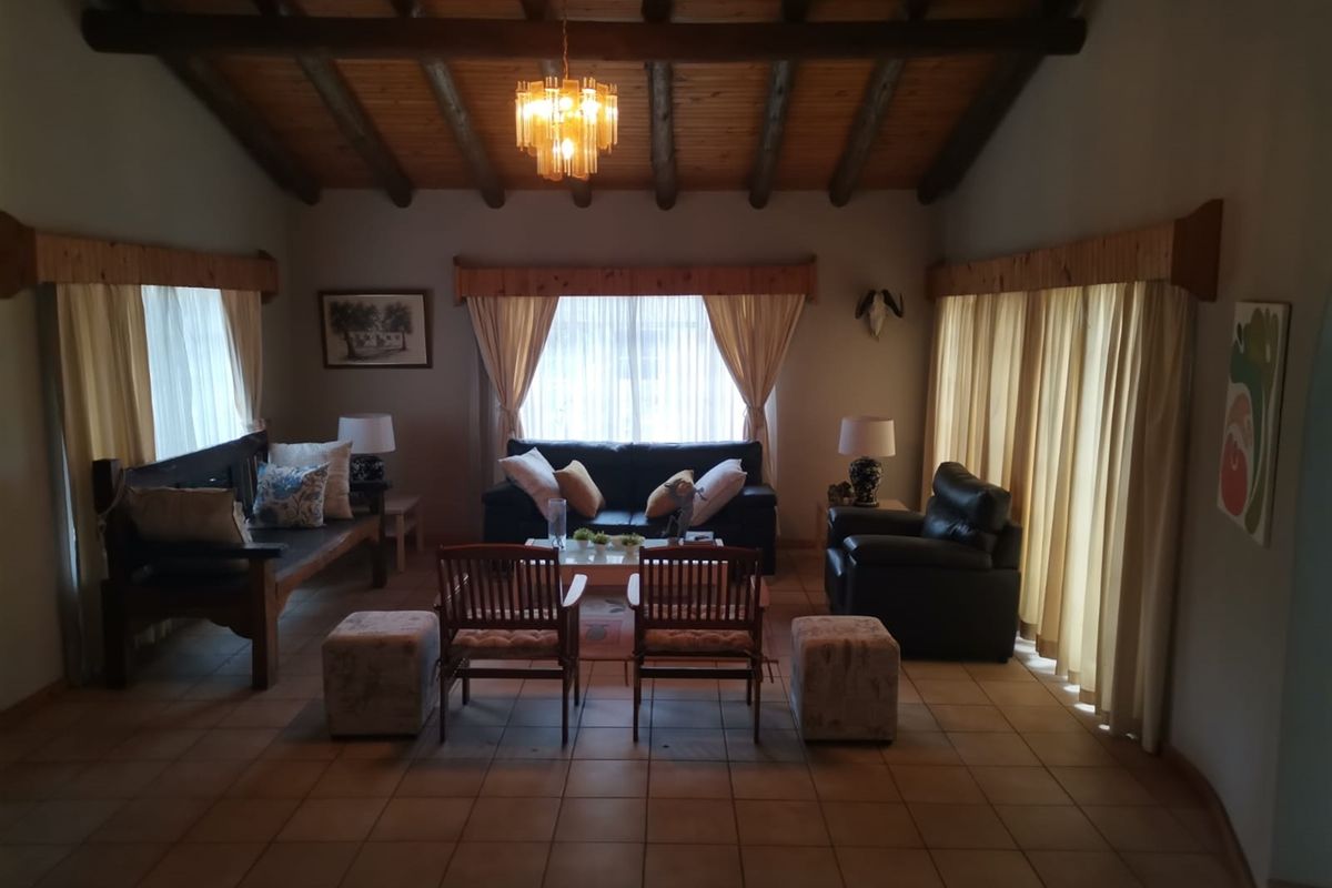 Spacious living room featuring a high exposed timber beam ceiling, ceramic tiled flooring, and large windows with timber pelmets.
