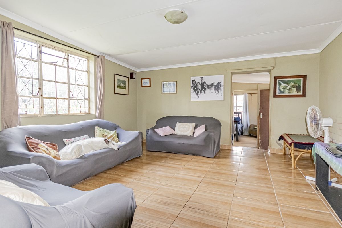 A living room featuring tiled flooring and large windows with security bars, offering a functional space with potential for cosmetic updates.