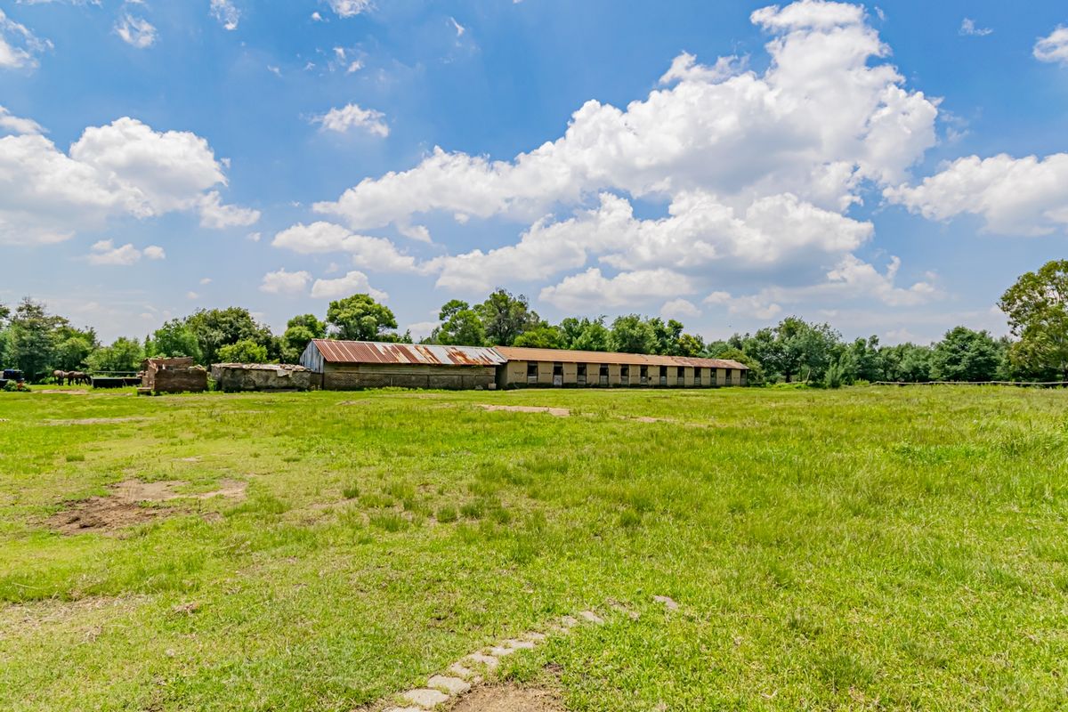 A wide view of the small holding grounds featuring a long stable block with a weathered corrugated metal roof set within open pasture land.