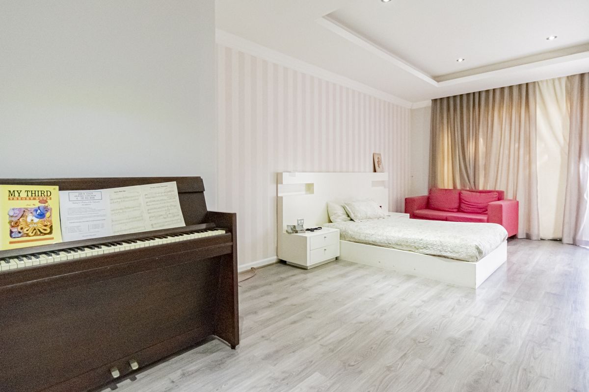 Spacious bedroom featuring modern laminate flooring, a recessed ceiling with downlights, and a custom built-in headboard with integrated bedside tables.