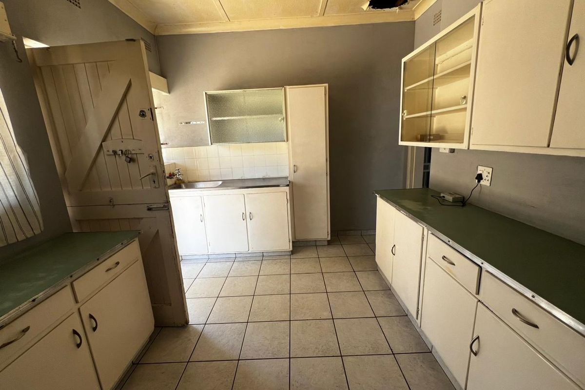 A dated kitchen featuring original built-in cabinetry, laminate countertops, and tiled flooring, currently requiring ceiling repairs and cosmetic updates.