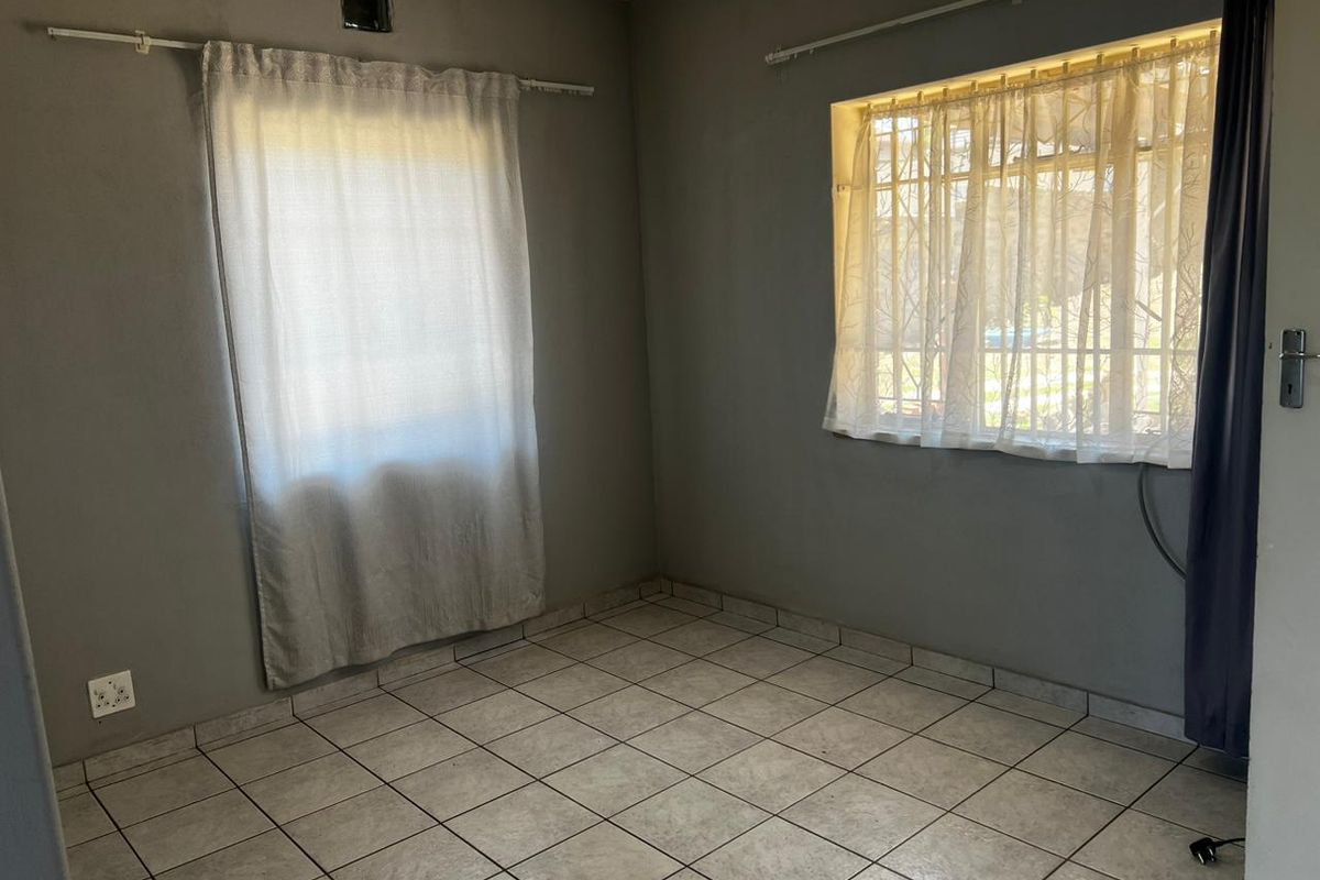 An empty bedroom featuring ceramic floor tiles, security bars on the windows, and neutral grey wall paint.