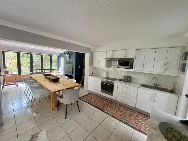 Open-plan kitchen and dining area featuring white cabinetry, integrated appliances, tiled flooring, and direct access to a covered patio through sliding glass doors.