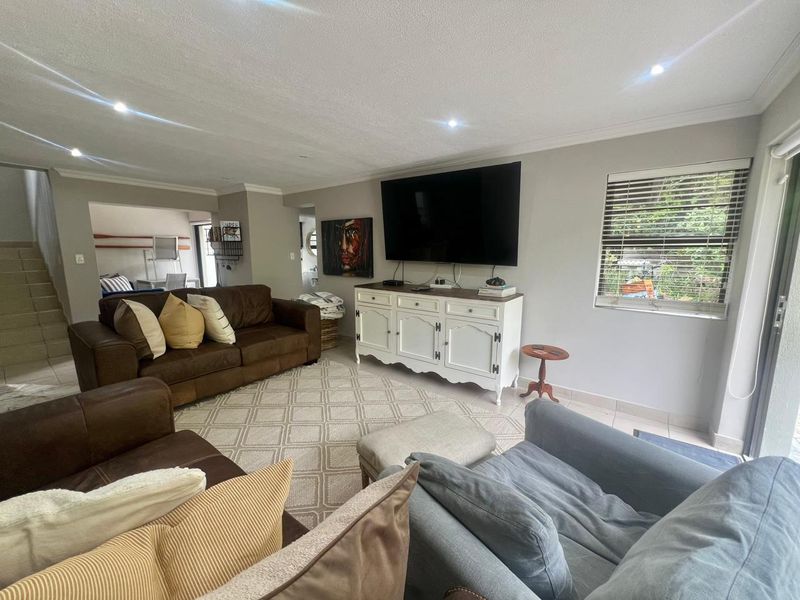 A spacious living room featuring neutral tiled flooring, recessed downlighting, and large sliding glass doors that provide natural light and garden access.