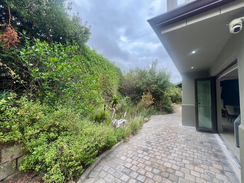 A paved outdoor patio area featuring recessed lighting, security camera, and bi-fold doors leading into the interior living space.
