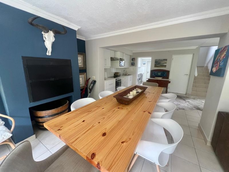 Open-plan dining area featuring a built-in fireplace and direct flow into a functional kitchen with white cabinetry and tiled flooring.