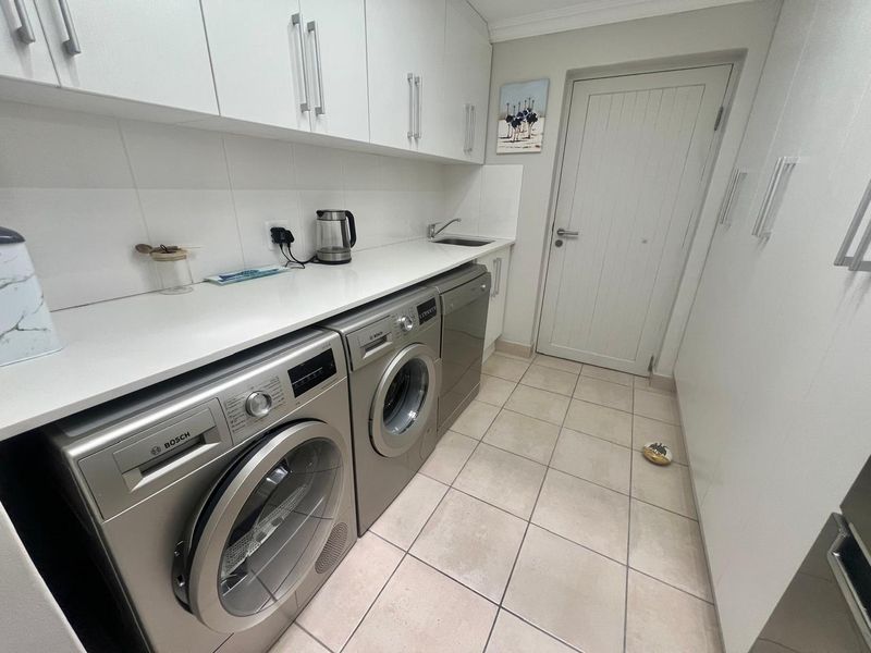 A clean and functional laundry room featuring white built-in cabinetry, stone-look countertops, an integrated sink, and tiled flooring.