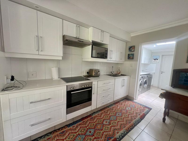Modern kitchen featuring white cabinetry, integrated appliances, and a tiled floor, with an adjacent laundry area visible through the doorway.
