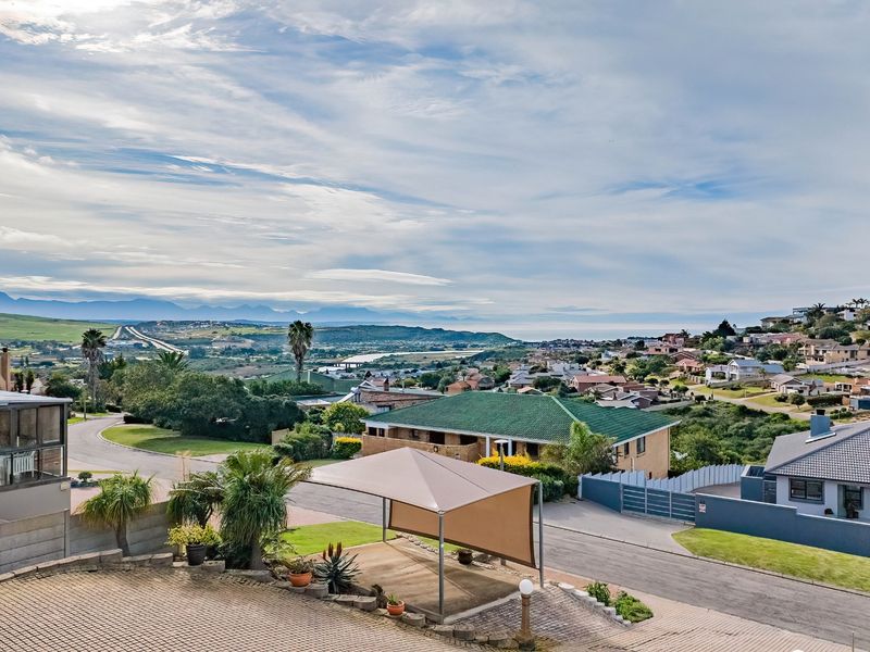 Elevated view overlooking the surrounding residential neighbourhood, featuring a paved driveway, shade sail structure, and distant mountain and coastal landscape.
