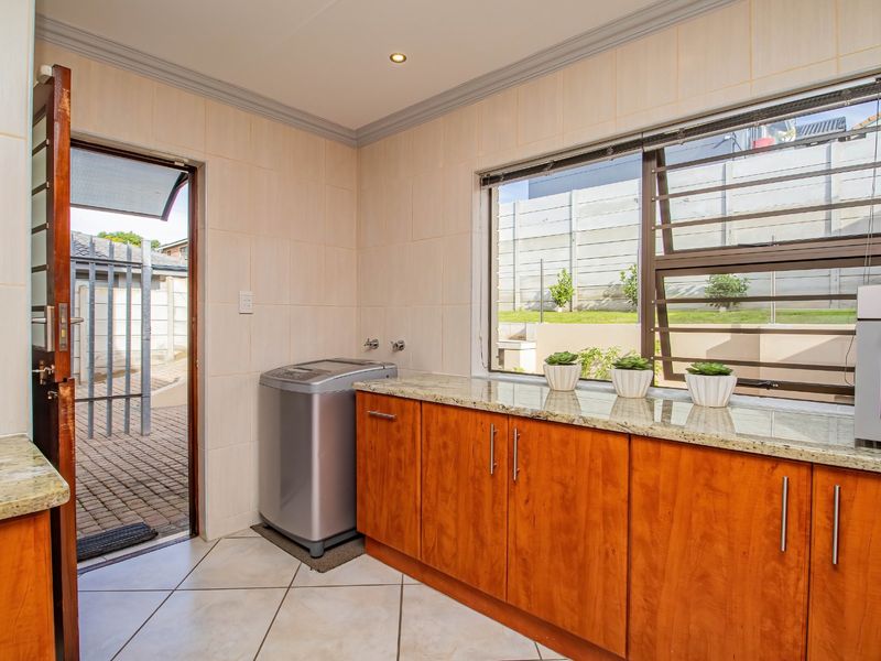 A functional laundry room featuring granite countertops, wooden cabinetry, tiled finishes, and direct access to the exterior patio area.
