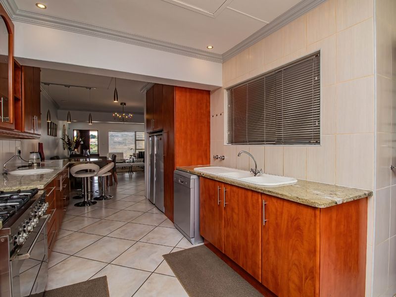Open-plan kitchen featuring warm wood cabinetry, granite countertops, gas hob, and tiled flooring, seamlessly flowing into the adjacent dining and living area.