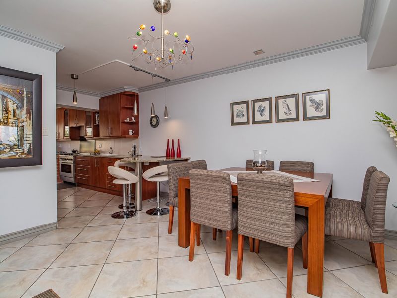 Open-plan dining and kitchen area featuring wooden cabinetry, stone countertops, a breakfast bar, and ceramic tiled flooring with decorative crown molding.