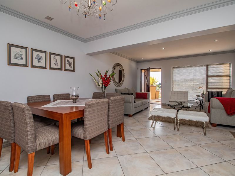 Spacious open-plan living and dining area featuring tiled flooring, crown molding, and natural light through large windows with venetian blinds.