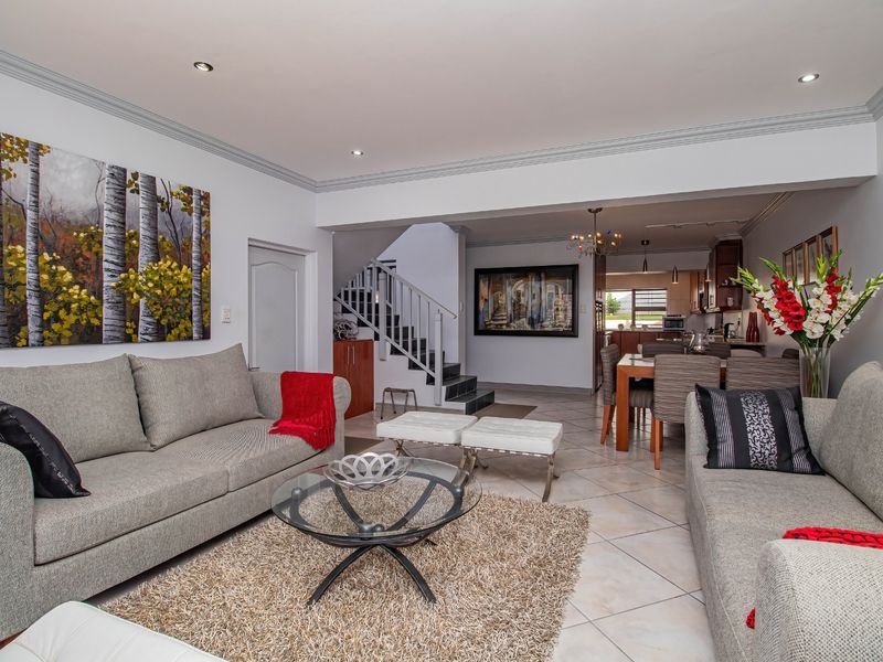 Spacious open-plan living and dining area featuring tiled floors, recessed lighting, crown molding, and an integrated staircase leading to the upper level.
