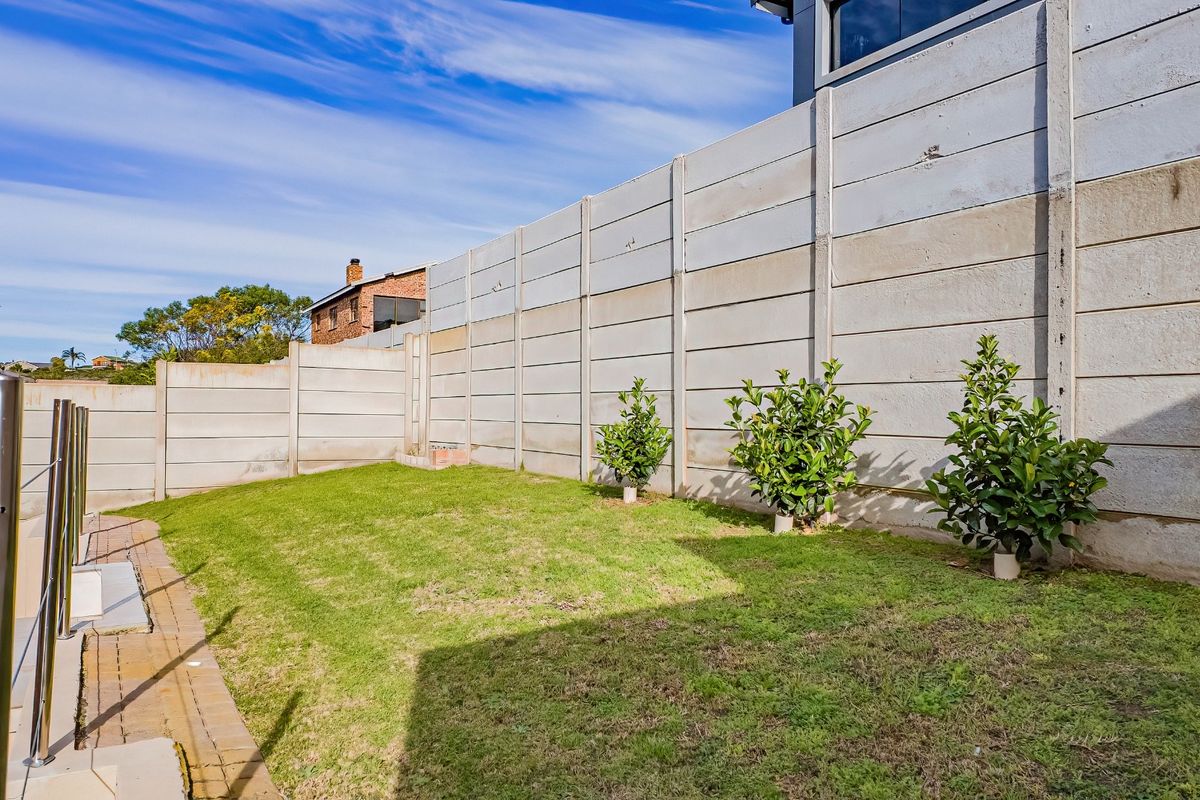 A rear garden area featuring a lawn, paved walkway, and a high precast concrete boundary wall providing privacy.