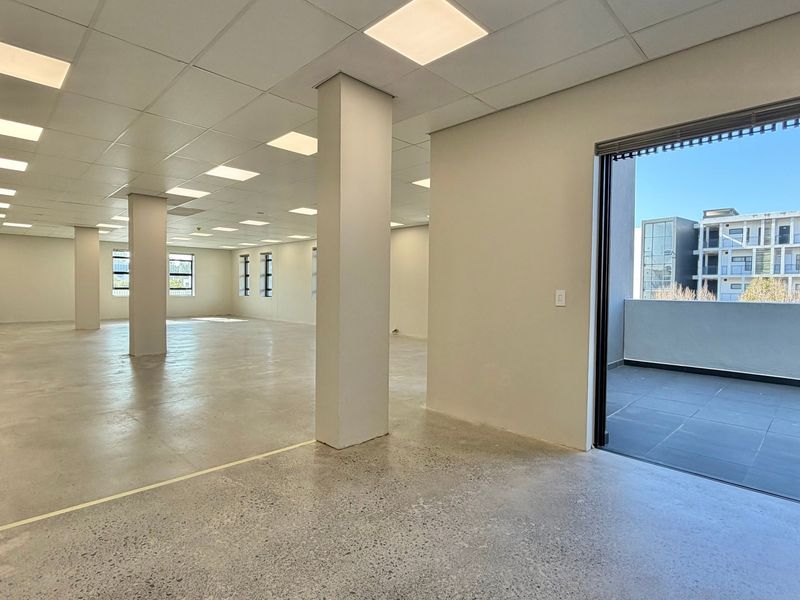 Spacious open-plan commercial office area featuring polished concrete floors, suspended ceilings with recessed lighting, and direct access to a private balcony.