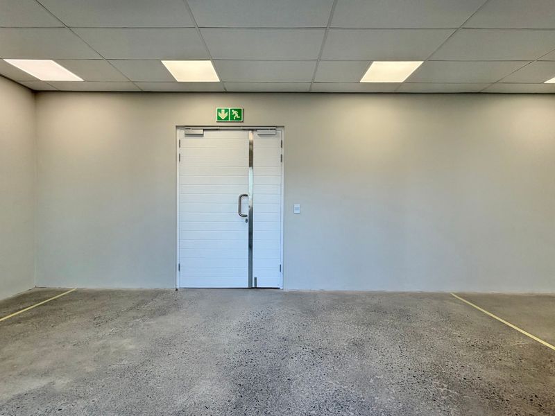 A clean, minimalist utility space featuring polished concrete flooring, a suspended ceiling with recessed lighting, and a secure double fire exit door.