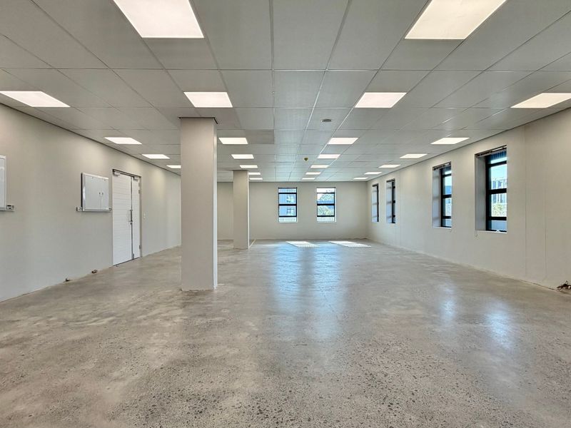 A spacious, open-plan commercial office area featuring polished concrete floors, a suspended ceiling with recessed lighting, and large windows providing natural light.