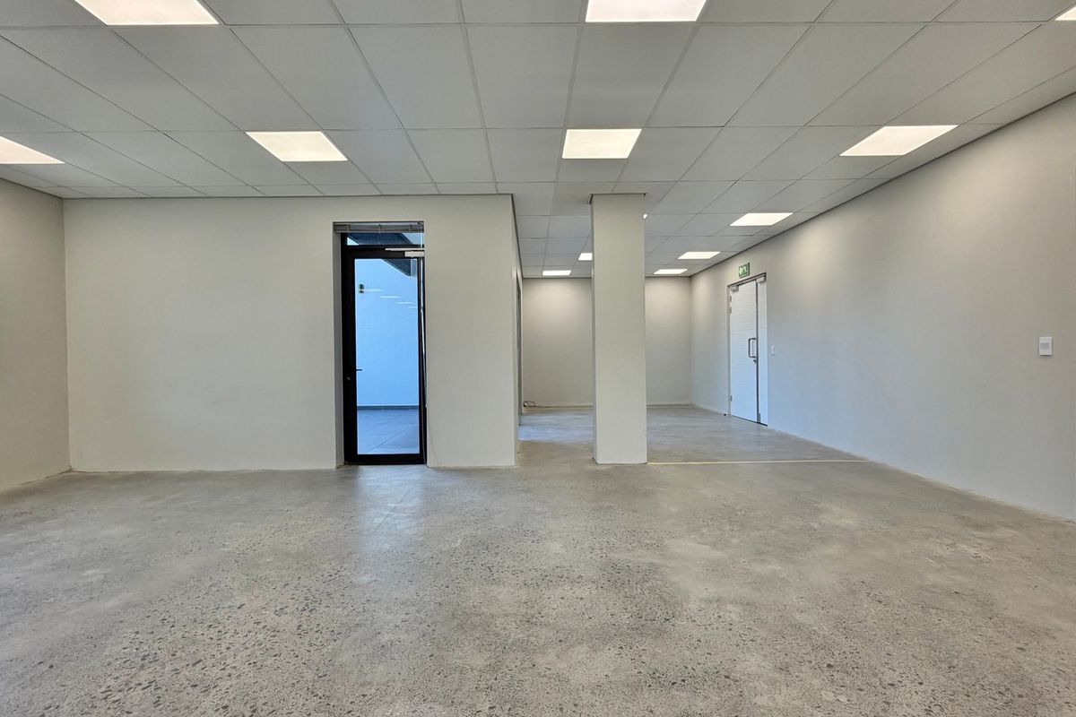 A spacious, modern open-plan commercial office area featuring polished concrete floors, a suspended ceiling with recessed lighting, and clean white walls.