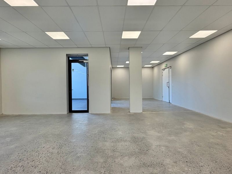 A spacious, modern open-plan commercial office area featuring polished concrete floors, a suspended ceiling with recessed lighting, and clean white walls.
