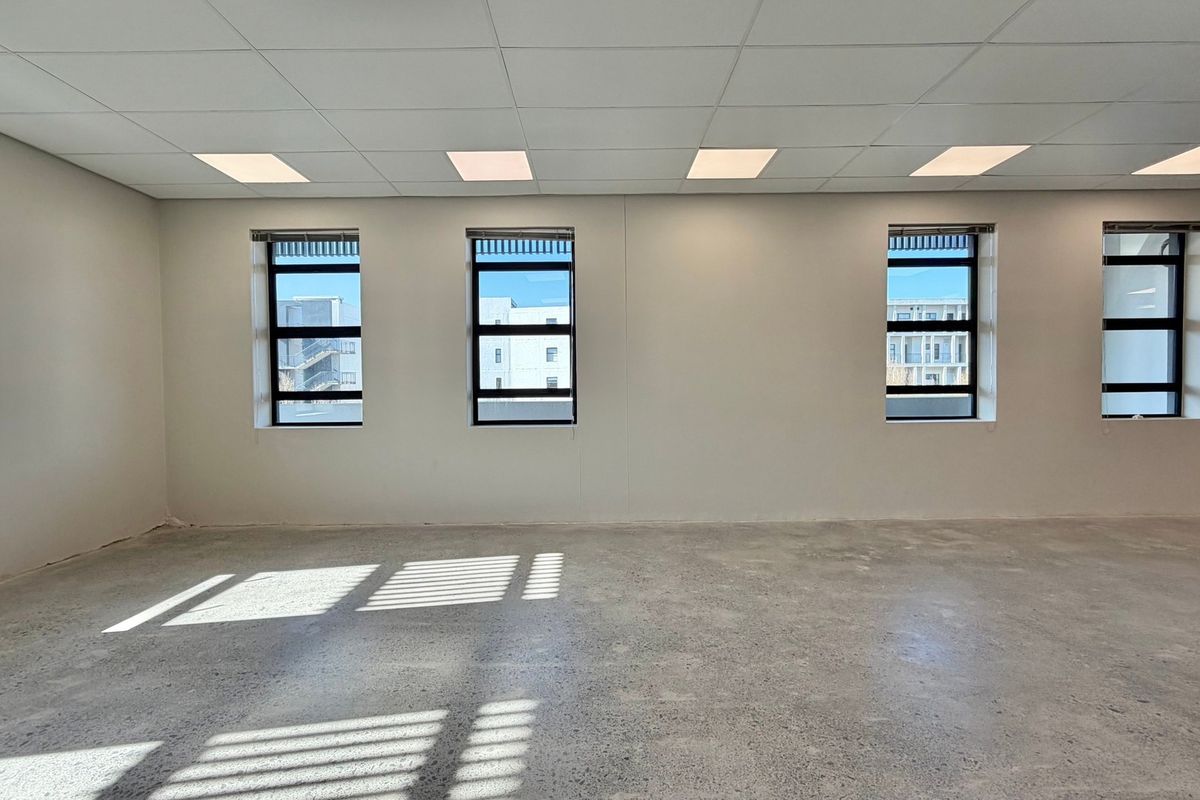 A bright, open-plan commercial office space featuring polished concrete floors, a suspended ceiling with recessed lighting, and large windows providing natural light.