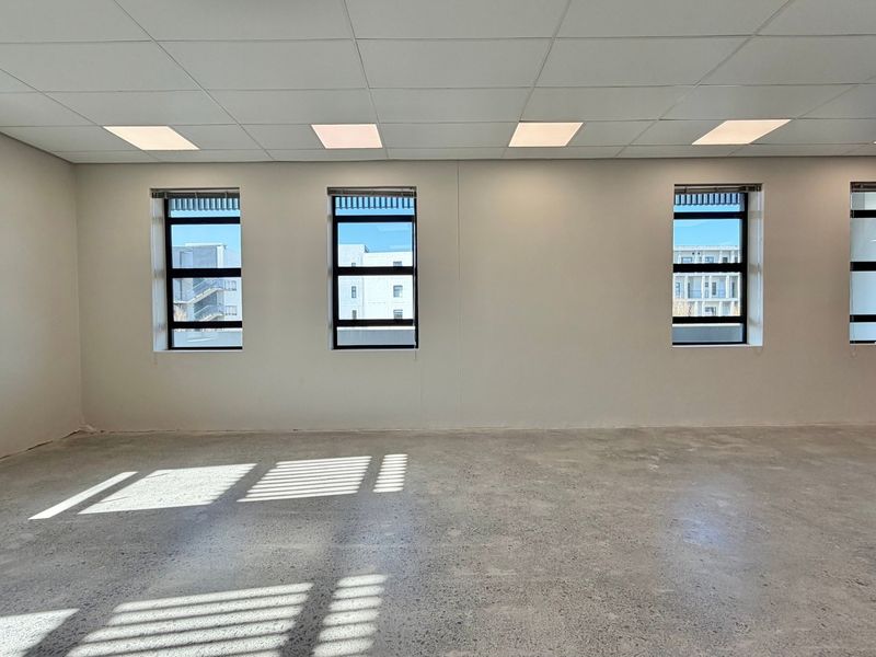 A bright, open-plan commercial office space featuring polished concrete floors, a suspended ceiling with recessed lighting, and large windows providing natural light.