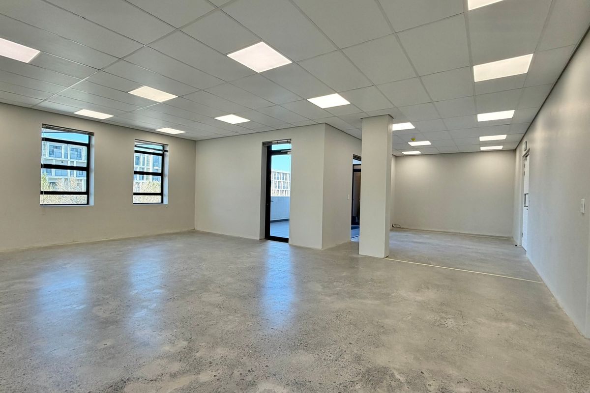 A spacious, modern open-plan office area featuring polished concrete floors, a suspended ceiling with recessed LED lighting, and large windows providing ample natural light.
