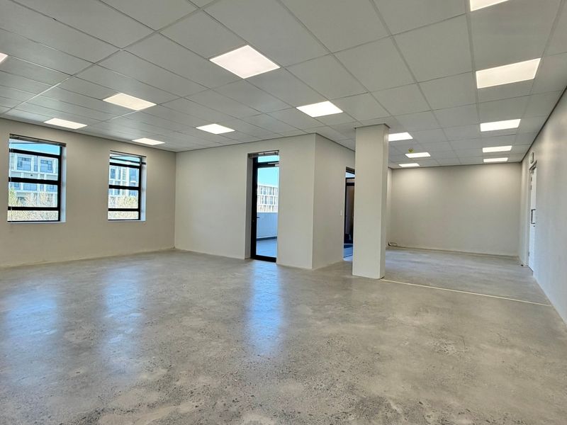 A spacious, modern open-plan office area featuring polished concrete floors, a suspended ceiling with recessed LED lighting, and large windows providing ample natural light.