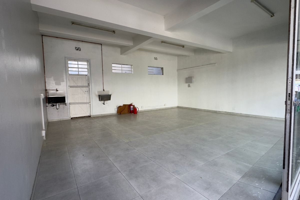 An empty, functional commercial kitchen space featuring tiled flooring, wall-mounted stainless steel sinks, and exposed utility piping, ready for custom fit-out.